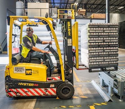 pexels-photo-1267338-1267338 A warehouse worker maneuvers a forklift to transport crates for brewing company storage.